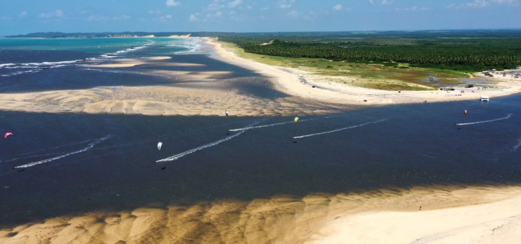 Foto de drone da Barra do Cunhaú mostrando pessoas praticando esportes aquáticos.