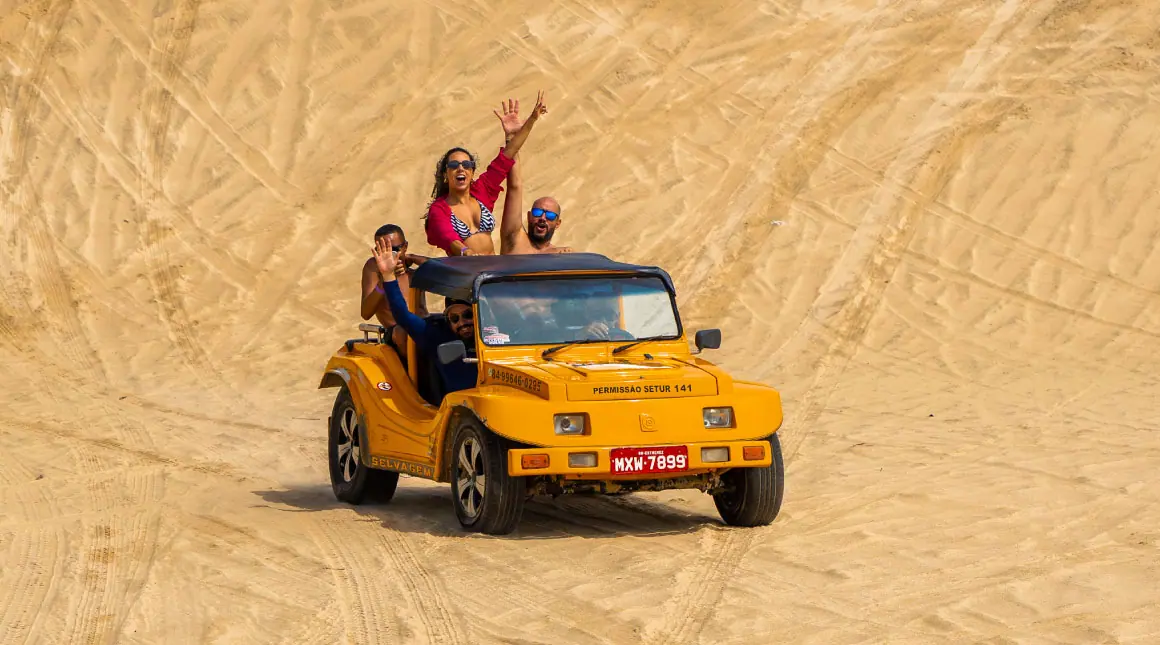 Grupo de amigos se divertindo em um passeio de buggy nas dunas de areia, representando a adrenalina e a aventura das atividades ao ar livre no Esmeralda Praia Hotel.