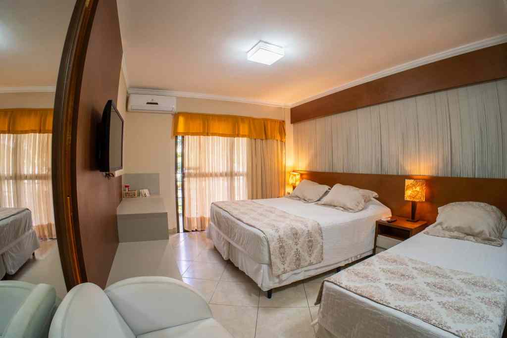Apartamento do Esmeralda Praia Hotel com cama de casal, poltronas, varanda com vista para o mar e decoração em tons claros e detalhes em madeira.