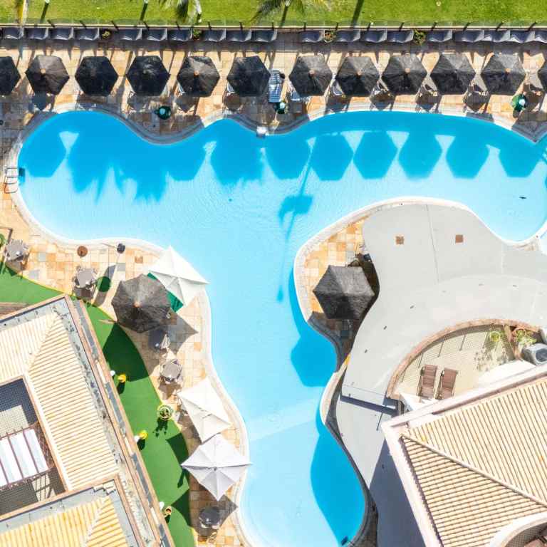 Imagem aérea mostra a ampla piscina com espreguiçadeiras e quiosques do Esmeralda Praia Hotel, resort à beira-mar em Natal RN