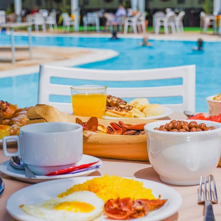 Mesa de café da manhã com ovos, frutas, pães, café e suco servidos à beira da piscina do Esmeralda Praia Hotel em Natal Rio Grande do Norte