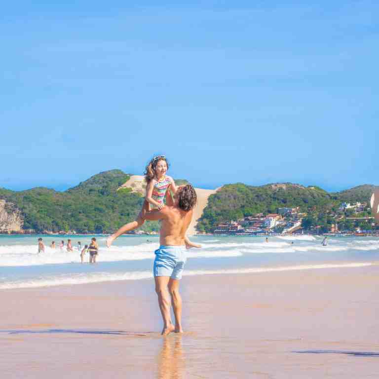 Turistas aproveitando dia ensolarado na Praia de Ponta Negra com o Morro do Careca ao fundo em Natal RN