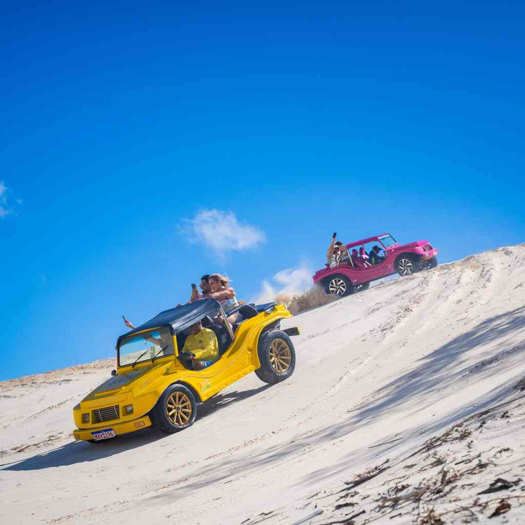 Turistas se divertindo em buggies coloridos descendo as dunas de Genipabu, uma das principais atrações de Natal RN