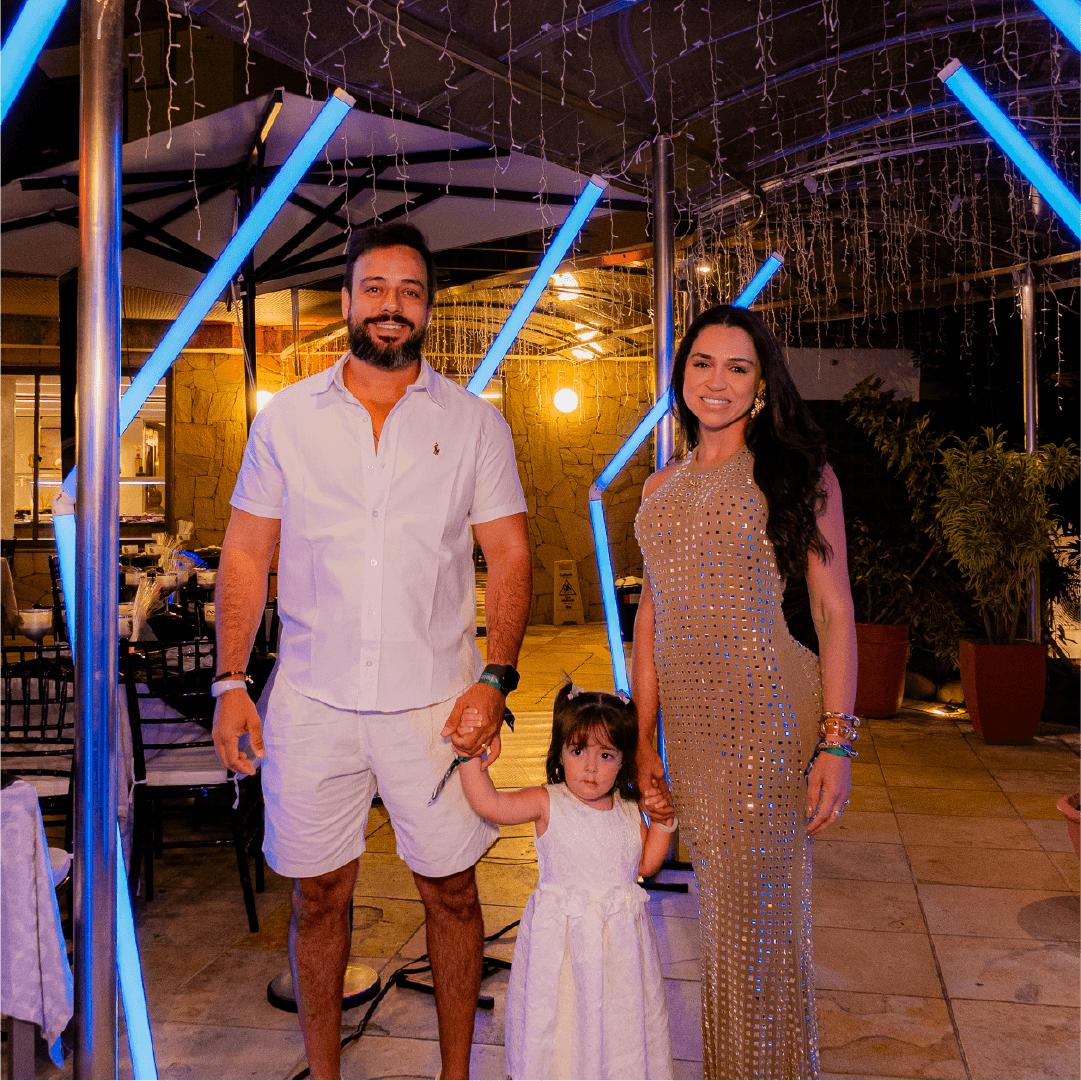 Casal com filha pequena em traje branco na área decorada do Réveillon Esmeralda, em Natal